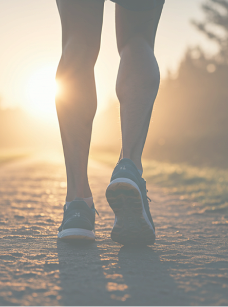 Person walking on a path with legs and shoes visible, sun setting in the background - Athletic Recovery