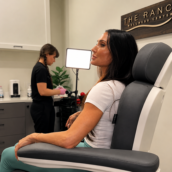 Woman receiving a facial treatment in a spa setting with 'The Ranc Wellness Center' sign.